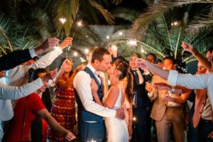 Portait des mariés entourés par les invités sous les bougies étincelantes sparkles sous les palmiers du château de garde